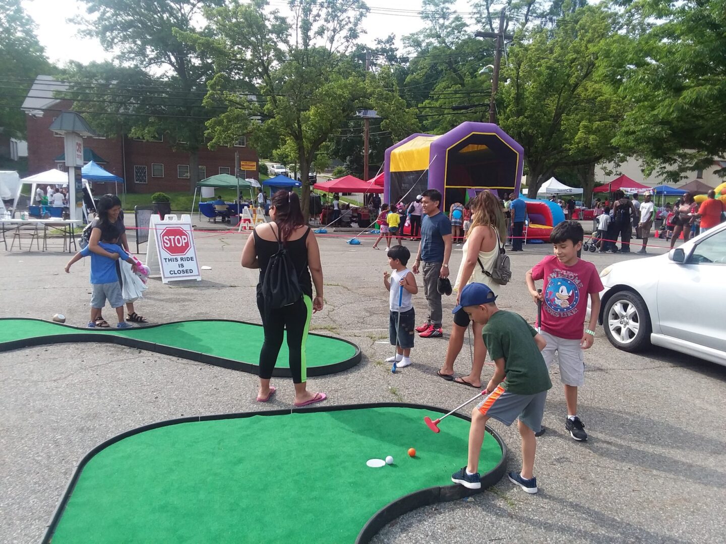 A group of people playing mini golf at an outdoor event.
